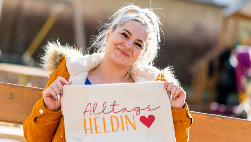 Frau hält Schild mit der Aufschrift: Alltagsheldin