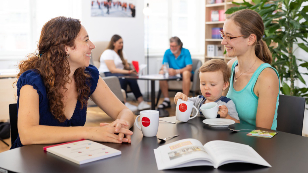 Frau mit Kind unterhält sich mit einer anderen Frau beim Kaffee- oder Teetrinken